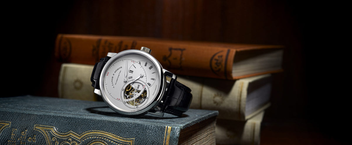 An A. Lange & Söhne tourbillon watch with a silver dial and black leather strap resting on a stack of antique books
