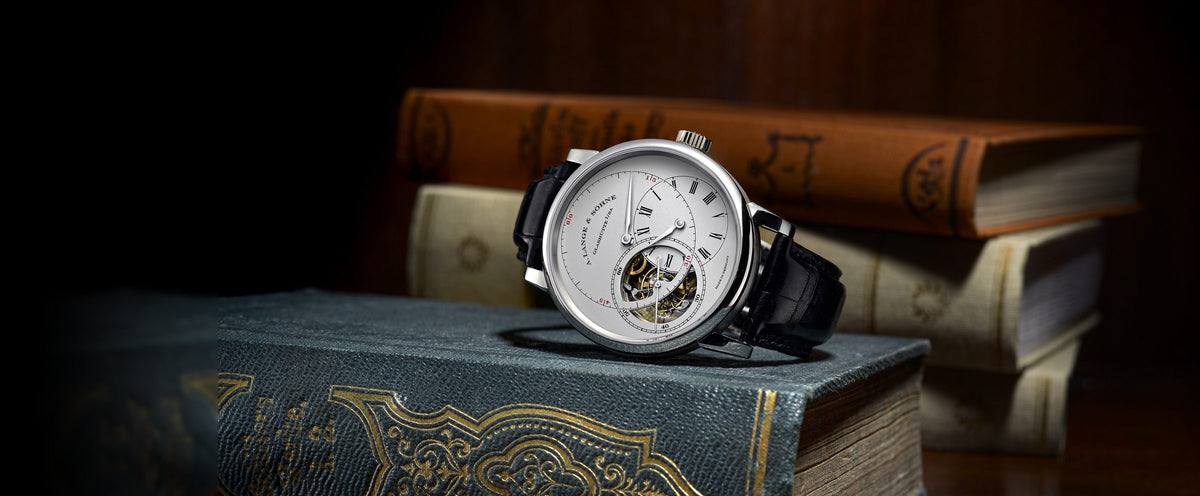 An A. Lange & Söhne tourbillon watch with a silver dial and black leather strap resting on a stack of antique books